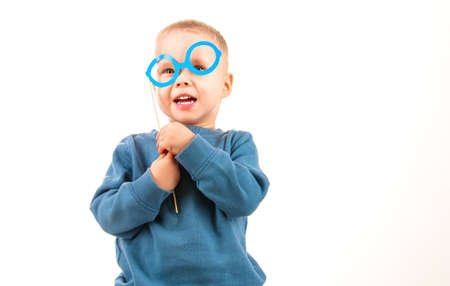 Happy little boy playing with paper glasses, laughing while doing face, on white background, fun for...