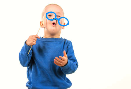 Happy little boy playing with paper glasses, laughing while doing face, on white background, fun for...