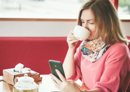 Portrait of an urban fashionable girl using a smartphone and with a cup of coffee in a cafe at a...