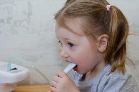 a little girl makes inhalation at home with an inhalerの写真素材