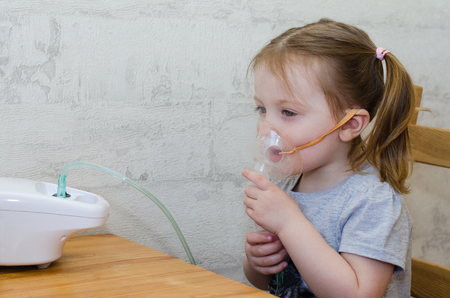 a little girl makes inhalation at home with an inhalerの写真素材