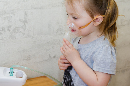 a little girl makes inhalation at home with an inhalerの写真素材
