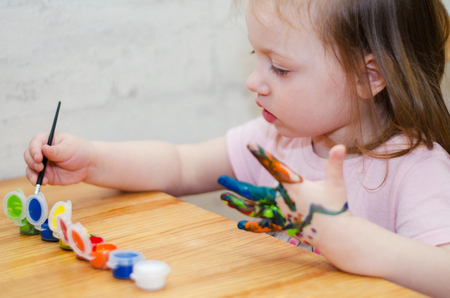 little girl paints her hands with colorful paintsの写真素材