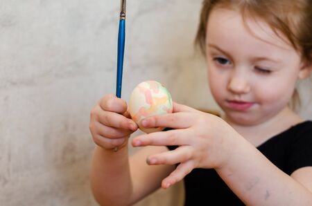 little girl paints an easter egg with a brush