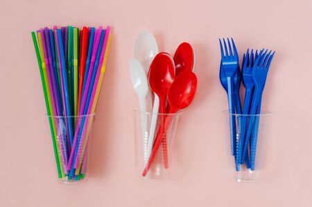 disposable plastic color cutlery and straws on a pink background, top viewの写真素材