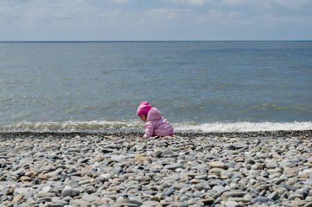 little funny girl on a stone beach at sea in springの写真素材