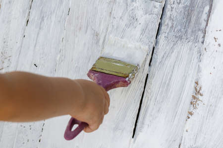 children's hand paints a wooden surface with white paint with a paint brushの写真素材