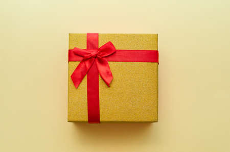 golden gift box with red bow on yellow background, merry christmasの写真素材