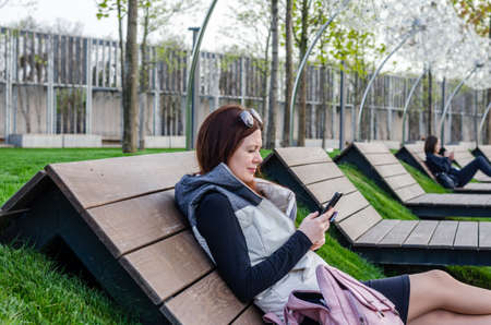 beautiful slender young white girl reads social networks from the phone outdoorsの写真素材
