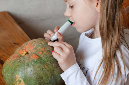 girl prepares pumpkin for halloween at the table. paints a scary face on a pumpkinの写真素材