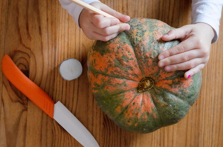 girl prepares pumpkin for halloween at the table. paints a scary face on a pumpkin. view from aboveの写真素材