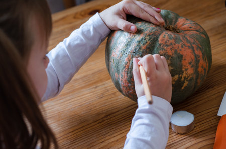 girl prepares pumpkin for halloween at the table. paints a scary face on a pumpkinの写真素材
