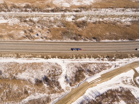 Snowy and frozen winter road with a moving car on it. Aerial view.