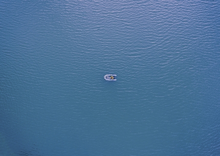 Fisherman catches a fish on a fishing boat. The beautiful bright water in a clear day. Aerial view from drone.の写真素材