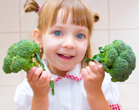 Portrait of a happy little girl with broccoli in kitchenの写真素材