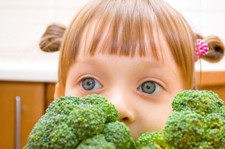 Portrait of a happy little girl with broccoli at kitchenの写真素材