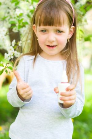 Portrait of a happy girl holding nasal spray,showing thumbs up outdoorsの写真素材