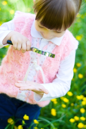 little girl is playing on green meadow examining hand using magnifying glassの写真素材
