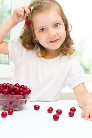 little girl with cherry berries bowl indoorsの写真素材