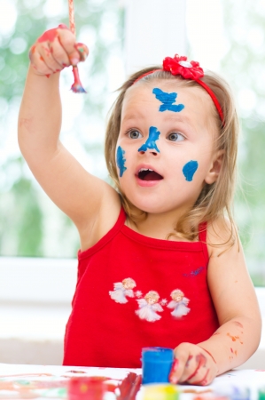 Cute little girl painting with paintbrush and colorful paintsの写真素材