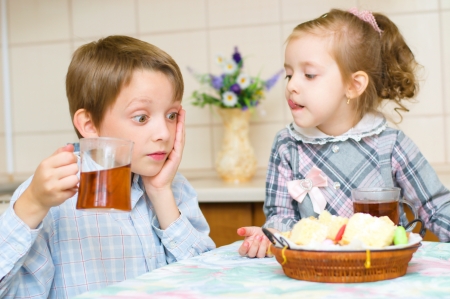 little girl with her brother sitting at the table drinking teaの写真素材