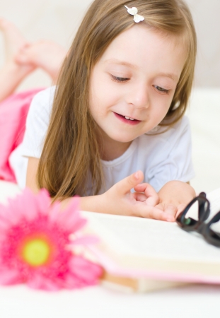 happy little girl is reading a book indoorsの写真素材