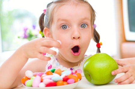 Cute little girl choosing between apples and  color sweetsの写真素材