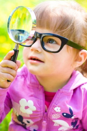 little girl is playing with magnifying glass on green meadowの写真素材