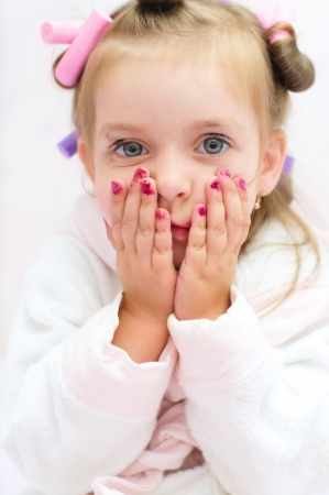 make-up,little girl is holding her face in astonishment while wearing hair-rollersの写真素材