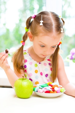 Cute little girl choosing between apple and color sweetsの写真素材