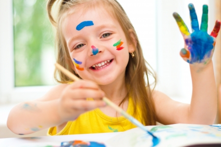 little girl painting with paintbrush and colorful paintsの写真素材