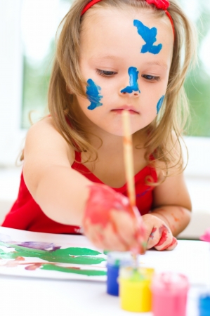 little girl painting with paintbrush and colorful paintsの写真素材