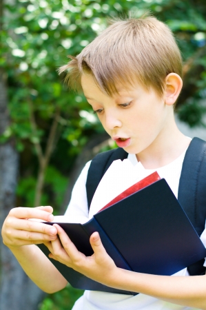 cute little schoolboy with backpack reading a book, outdoorsの写真素材