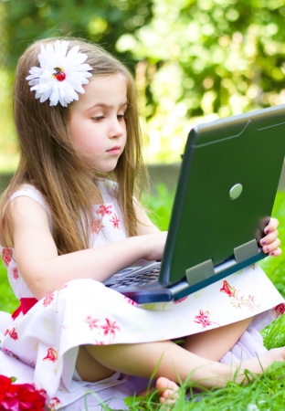 little girl using her laptop outdoor in park on grassの写真素材