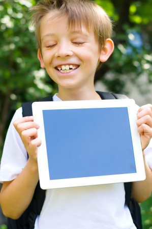 Happy little schoolboy with backpack and  tablet computer outdoorsの写真素材