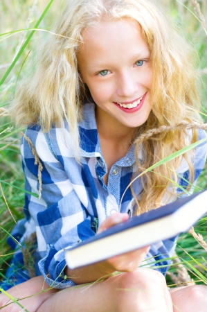 Young blond blue-eyed teenage girl sitting on the grass and holding a bookの写真素材