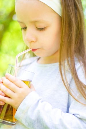 Cute little girl drinking apple juice outdoorsの写真素材