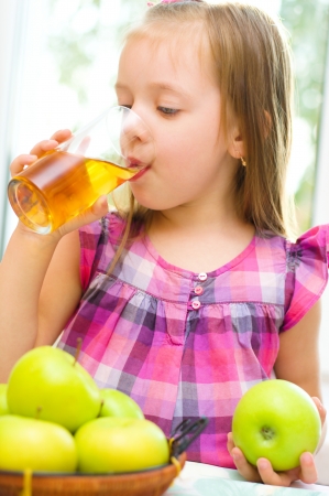 cute little girl holding green apple and drinking apple juiceの写真素材