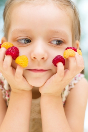 Happy little girl with raspberries at homeの写真素材