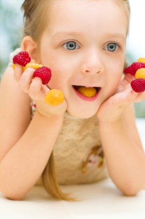 Happy little girl plays with raspberries at homeの写真素材