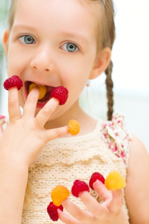 Happy little girl plays with raspberries at homeの写真素材