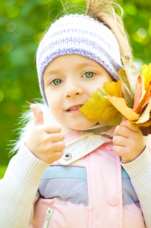 cute little girl with autumn leaves shows her thumb upの写真素材