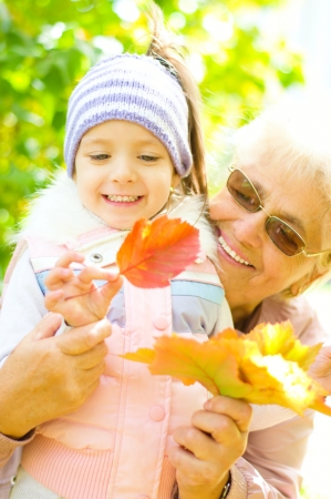 cute little girl with her great-grandmother holding autumn leavesの写真素材