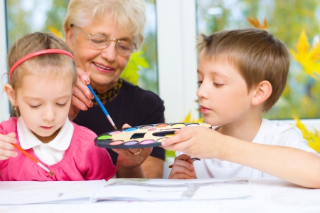 Grandmother with grandchildren painting with paintbrush and colorful paints, autumn backgroundの写真素材