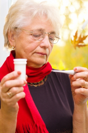 senior woman taking her temperature, autumn backgroundの写真素材