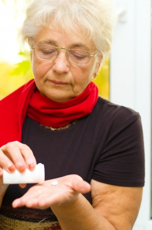 senior woman holding a pill in her hand, preparing to eat that - part of a series.の写真素材