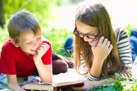 Kids reading together enjoying a book laying on the grass outdoorsの写真素材