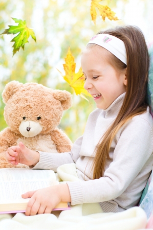 Cute little girl reading a book while sitting on the windowの写真素材