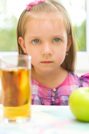 Sad little girl refuses to drink apple juiceの写真素材