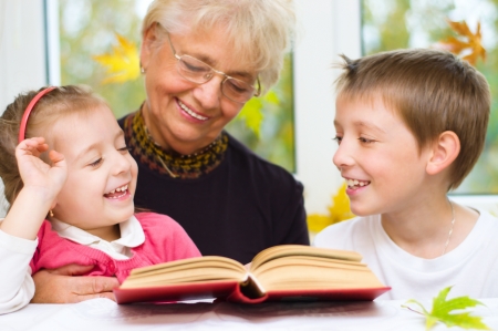 Great-grandmother reading a book for grandchildren at homeの写真素材